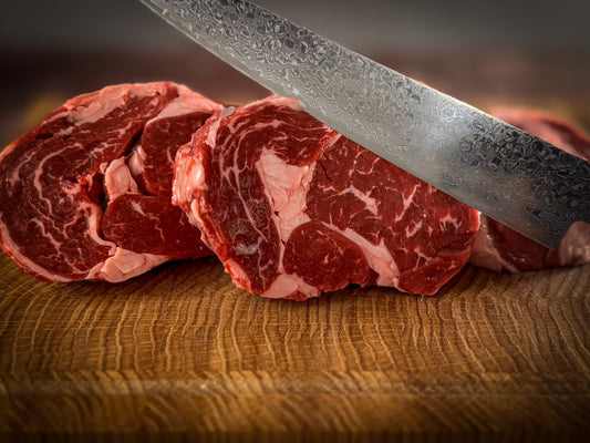 Frisch geschnittenes uruguayisches Bife Ancho (Ribeye) mit intensiver Marmorierung, angeschnitten mit einem handgeschmiedeten Damastmesser auf Holzbrett.