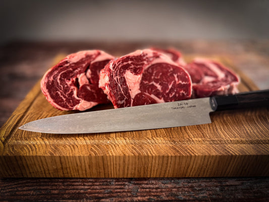 Ribeye Steak aus Uruguay, angerichtet auf Holzbrett mit japanischem Tamayuki-Messer – Symbol für Qualität und Handwerk.